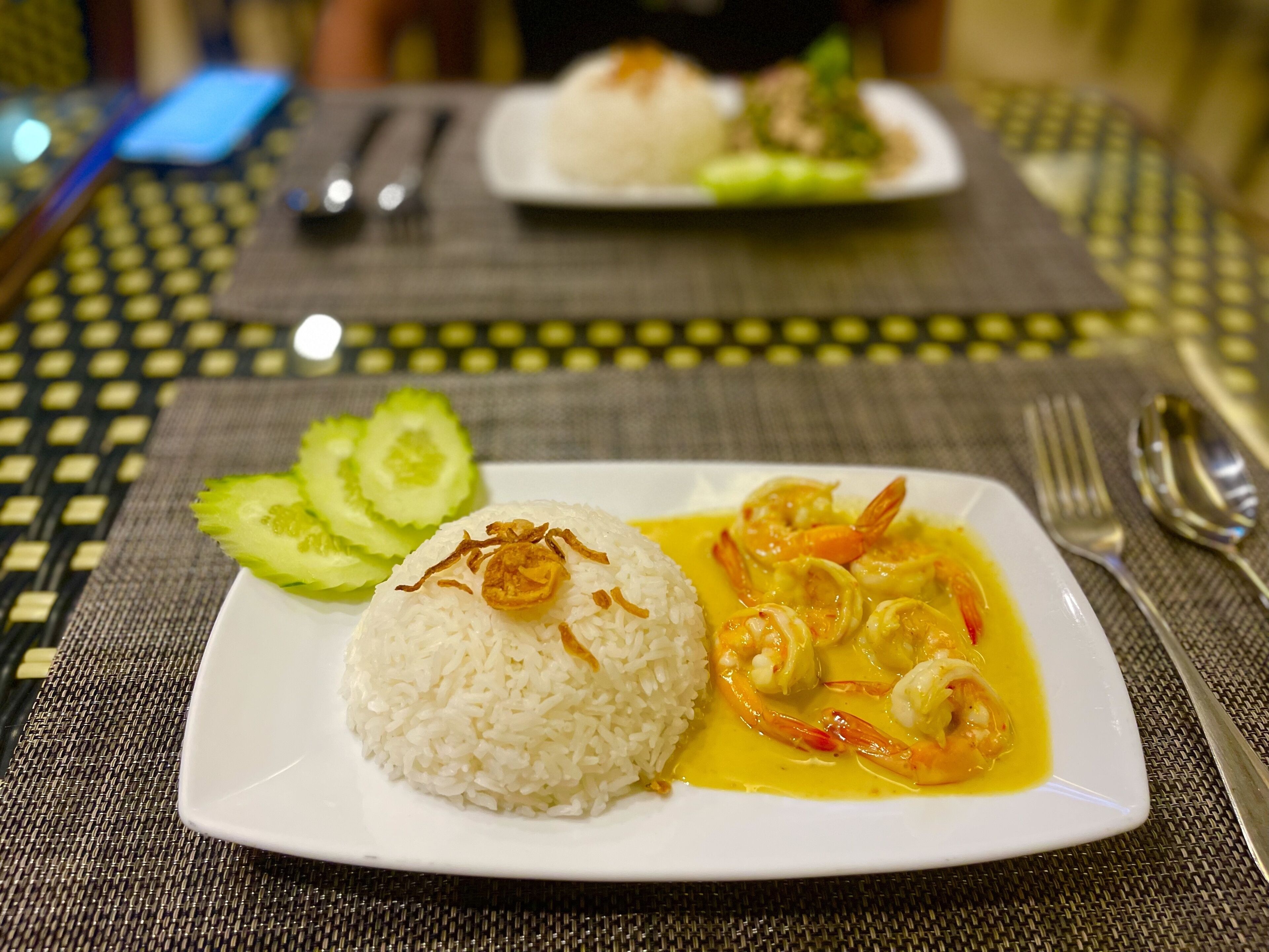 Un plato de arroz blanco con curry de camarones y rodajas de pepino sobre una mesa.
