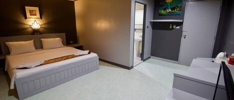 Habitación de hotel con una cama grande, un escritorio, una silla, un armario y un baño visible a través de una puerta abierta.