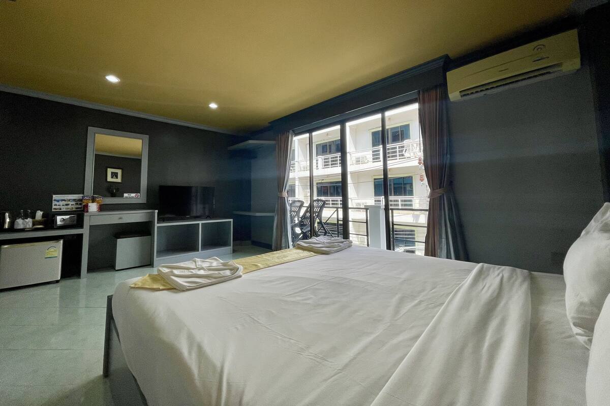 A hotel room with a bed, a desk, a TV, and a window with a view of a building.