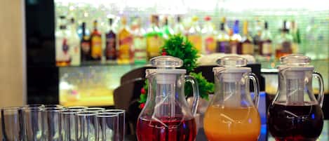 A bar area with several empty glasses lined up and three pitchers of different colored drinks on the counter.