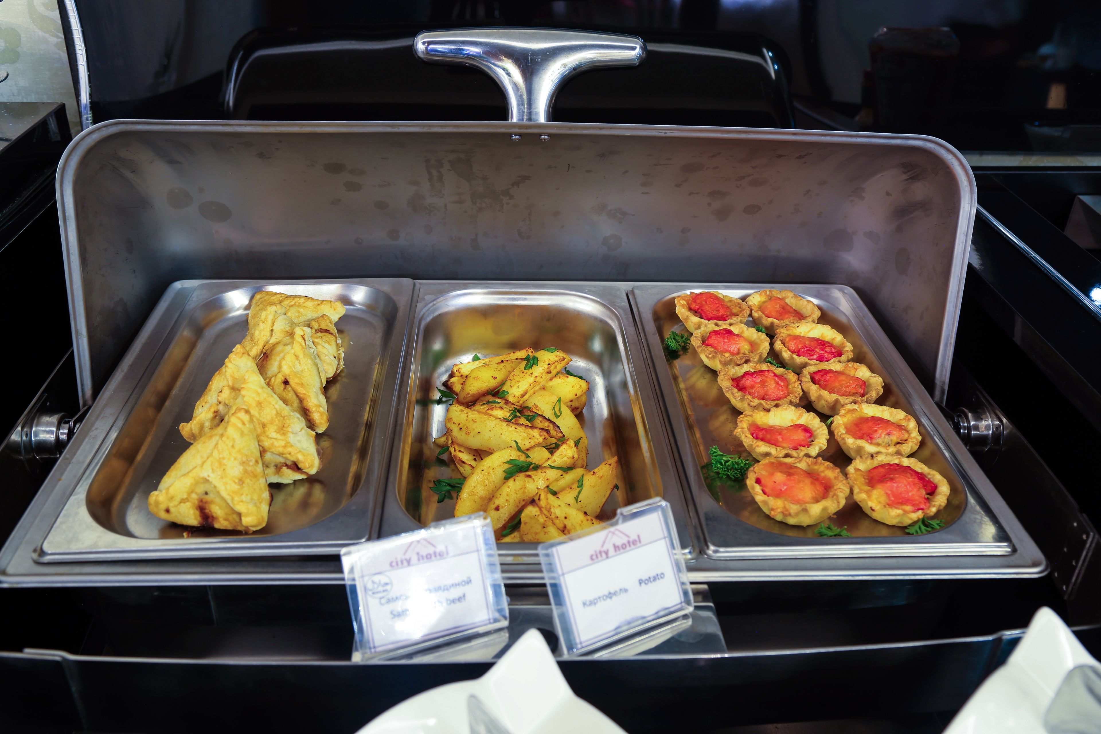 A buffet with trays of food including pastries, potato wedges, and quiches.
