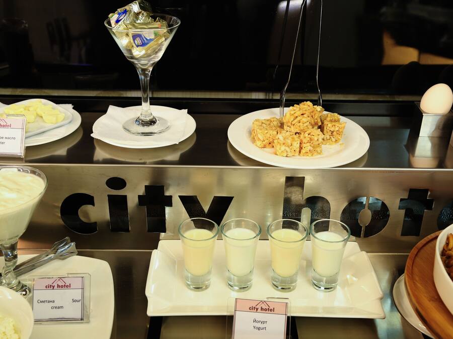 A buffet setup with various food items and beverages, including a martini glass, plates of butter, cream, and yogurt, and shot glasses filled with a creamy beverage.