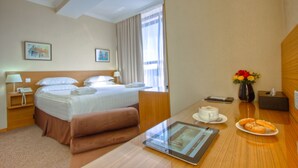 A hotel room with a bed, bedside tables, a desk with a tablet, a vase with flowers, and a coffee cup. - City Hotel Bishkek (Bishkek)