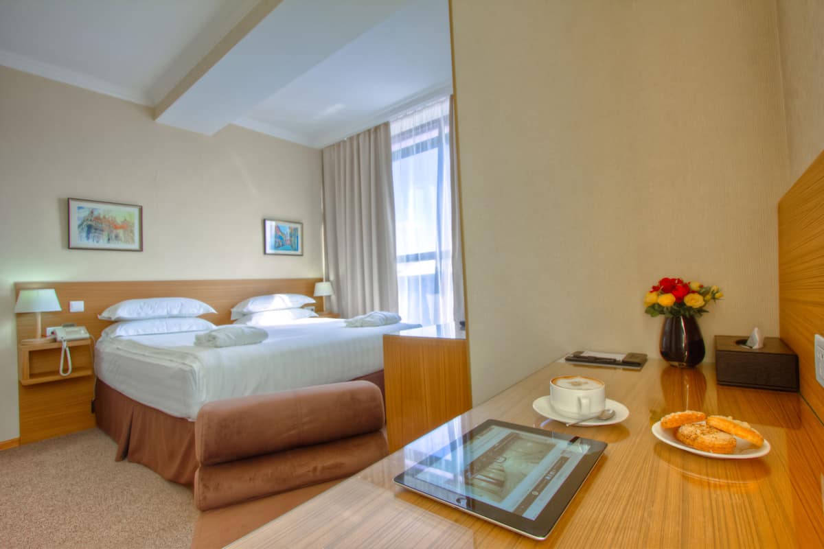 Een hotelkamer met een bed, nachtkastjes, een bureau met een tablet, een vaas met bloemen en een koffiekop.
