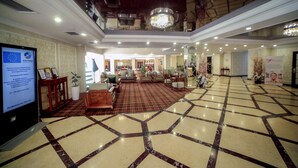 A spacious lobby with a checkered floor, a chandelier, and a television displaying a conference. - City Hotel Bishkek (Bishkek)