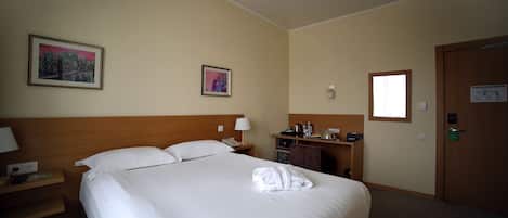 Une chambre d’hôtel avec un grand lit, un bureau avec une lampe, une petite armoire et deux tableaux encadrés au mur.