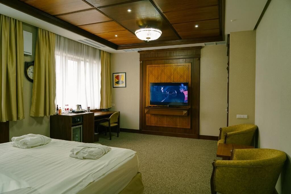 A hotel room with a bed, a desk with a chair, a television, and a clock on the wall.