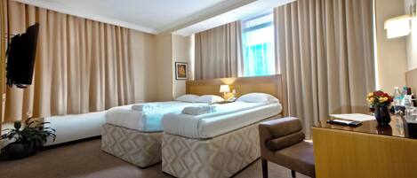 A hotel room with a bed, a desk, a chair, a TV, and a window with curtains.