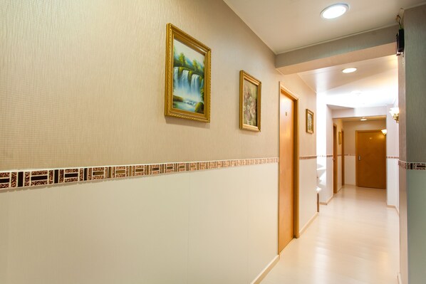 Corridoio di un albergo con bordatura piastrellata, opere d'arte incorniciate al muro e porte che conducono ad altre stanze.