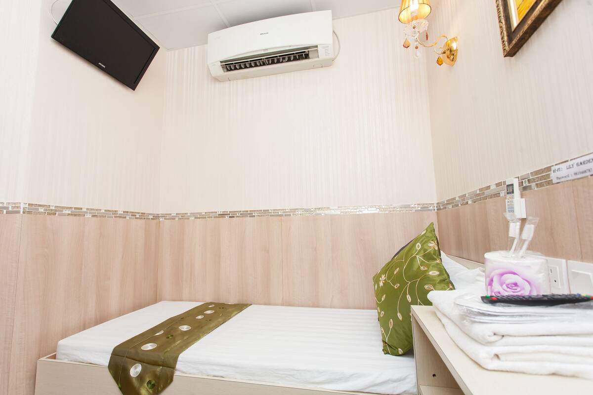 Habitación de hotel con cama, mesita de noche con artículos de aseo, aire acondicionado instalado en la pared y un televisor pequeño.