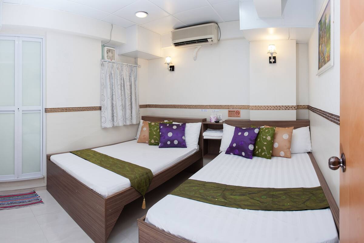 Habitación de hotel con dos camas, ventana con cortinas, unidad de aire acondicionado y una lámpara fijada a la pared.