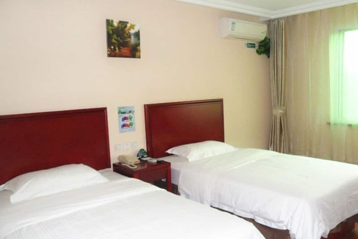 A hotel room with two single beds, a nightstand with a telephone, and a wall-mounted air conditioner.