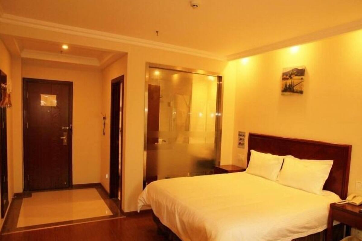 A hotel room with a bed, a nightstand, a telephone, and a door leading to a hallway.
