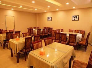 A hotel dining area with multiple round tables and chairs, each covered with a tablecloth.