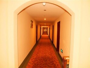 A long, narrow hotel hallway with a carpeted floor and doors on both sides.
