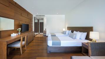A hotel room with a wooden desk, a television, two beds, a nightstand, and a lamp.
