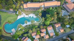 Vista aérea de uma área residencial com piscina, casas e um edifício grande com telhado vermelho.