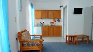 A small, cozy room with a wooden bed, a small table, and a kitchenette with wooden cabinets and a TV. - Kantaros Apartments (Corfu)