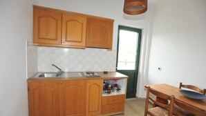 A kitchen with wooden cabinets, a sink, and a dining table with chairs. - Kantaros Apartments (Corfu)