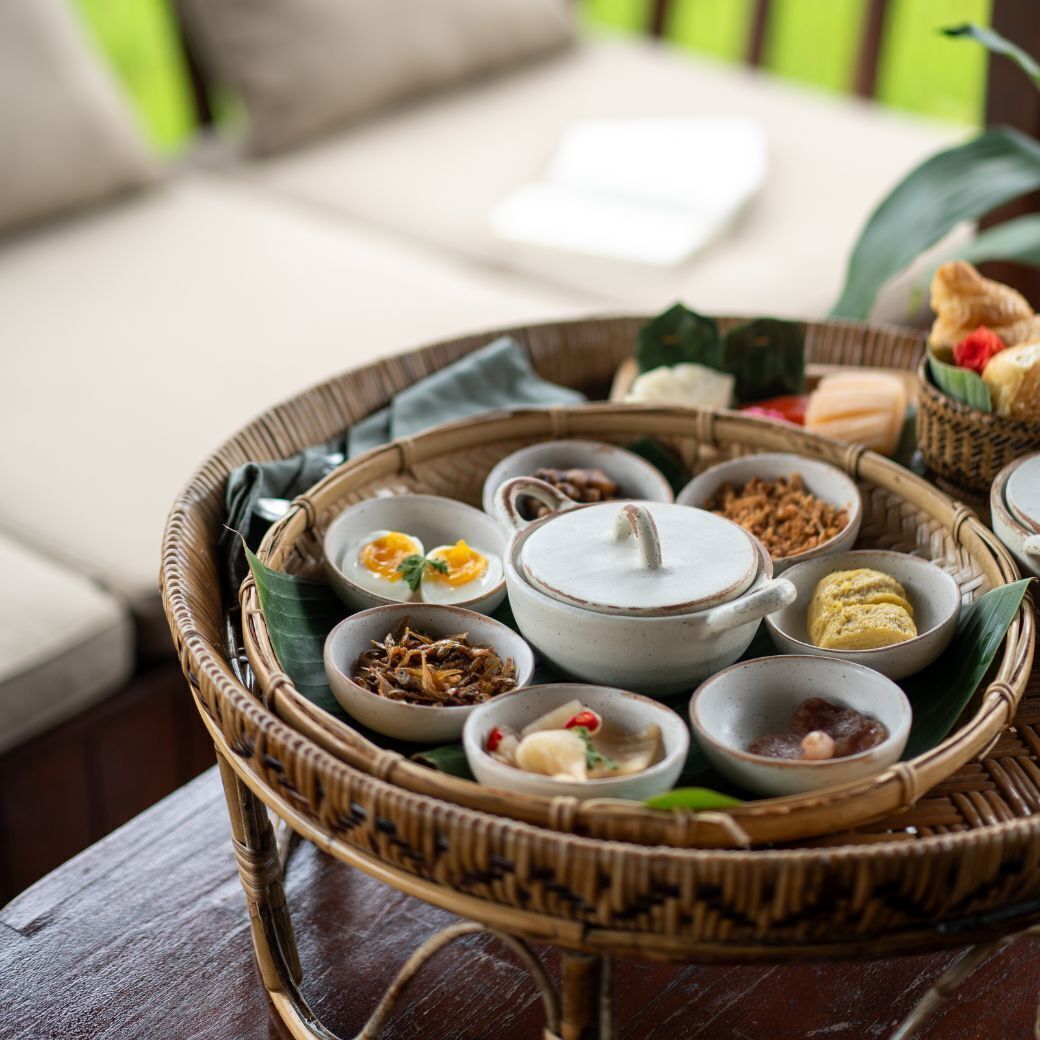 A wicker tray with various food items, including a bowl of soup, a dish with fried food, and several small bowls with different condiments.
