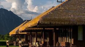 A row of thatched-roof cabins with wooden balconies, set in a lush green landscape with mountains in the background. - ViengTara VangVieng Resort (Vang Vieng)