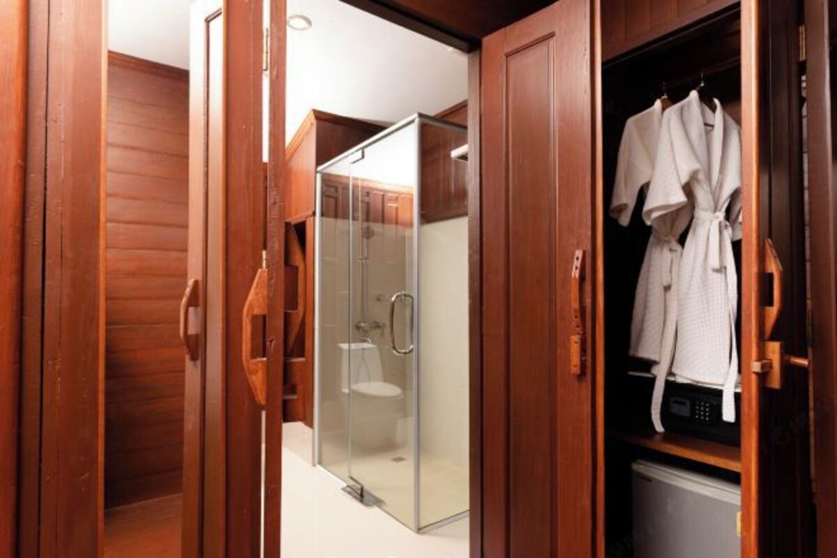 A wooden interior with a glass shower enclosure, a white toilet, and a robe hanging on a rack.