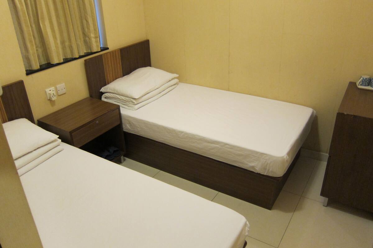 A hotel room with two single beds, a wooden nightstand, a small table, and a window with curtains.