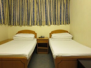A room with two single beds, wooden headboards, white bedding, a nightstand with a telephone, and a curtain with a blue and yellow pattern. - Hao's Inn (Kowloon)