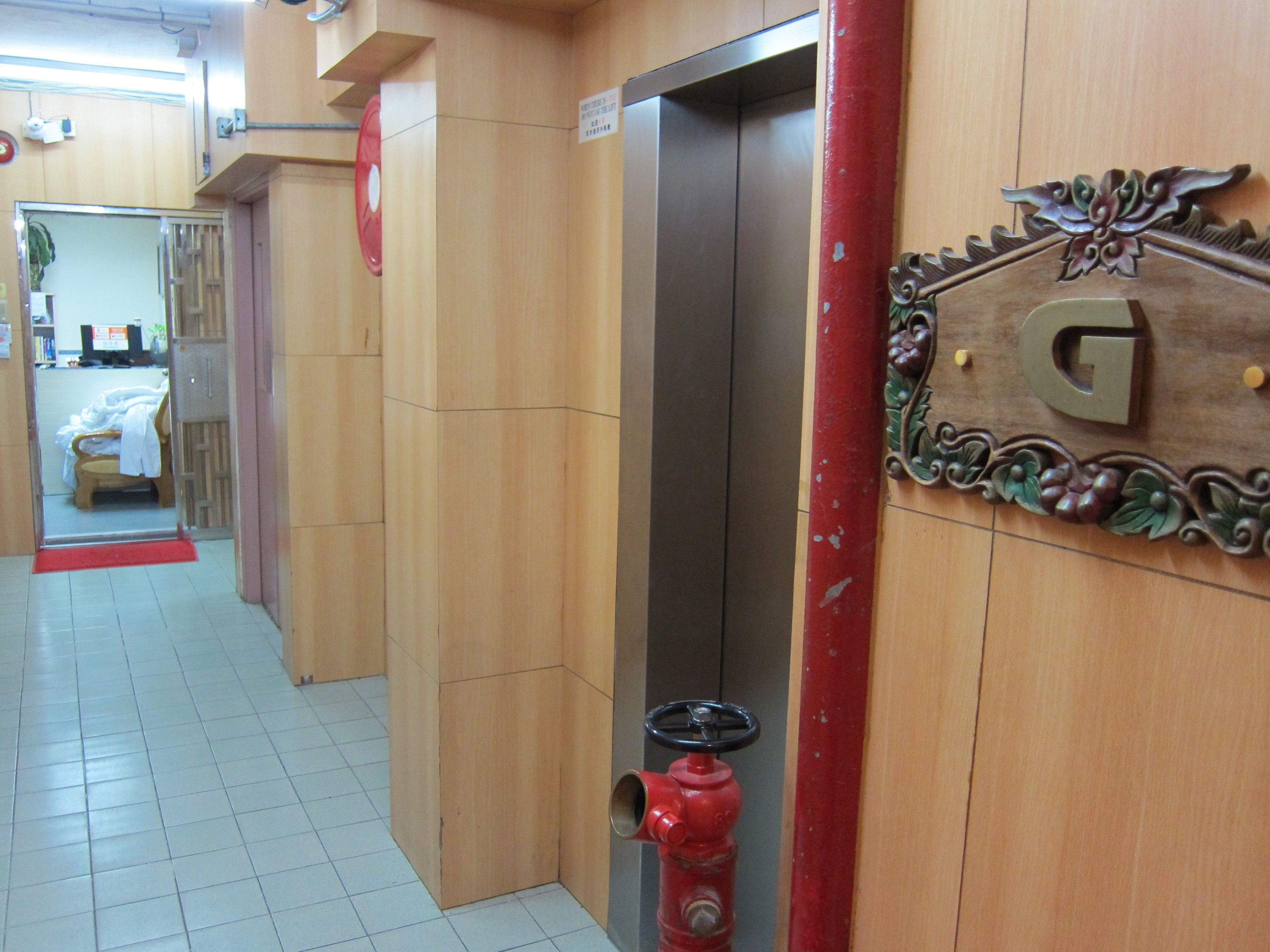 A hallway with a red fire hydrant, a wooden wall with a decorative sign, and an elevator.