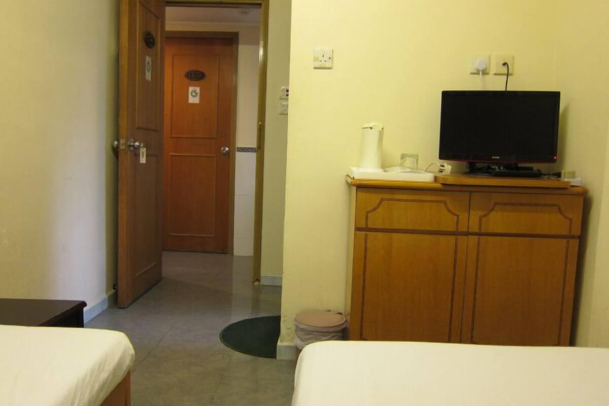 A hotel room with two beds, a wooden wardrobe, a television on a stand, and a door leading to another room.