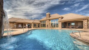 A swimming pool with a waterfall feature, surrounded by buildings with stone pillars and large windows. - Coral Springs Resort (Hurricane)