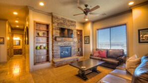 A living room with a stone fireplace, leather sofa, and a ceiling fan. - Coral Springs Resort (Hurricane)