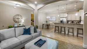 A spacious living room with a sofa, a coffee table, and a dining area with a chandelier. - Coral Springs Resort (Hurricane)