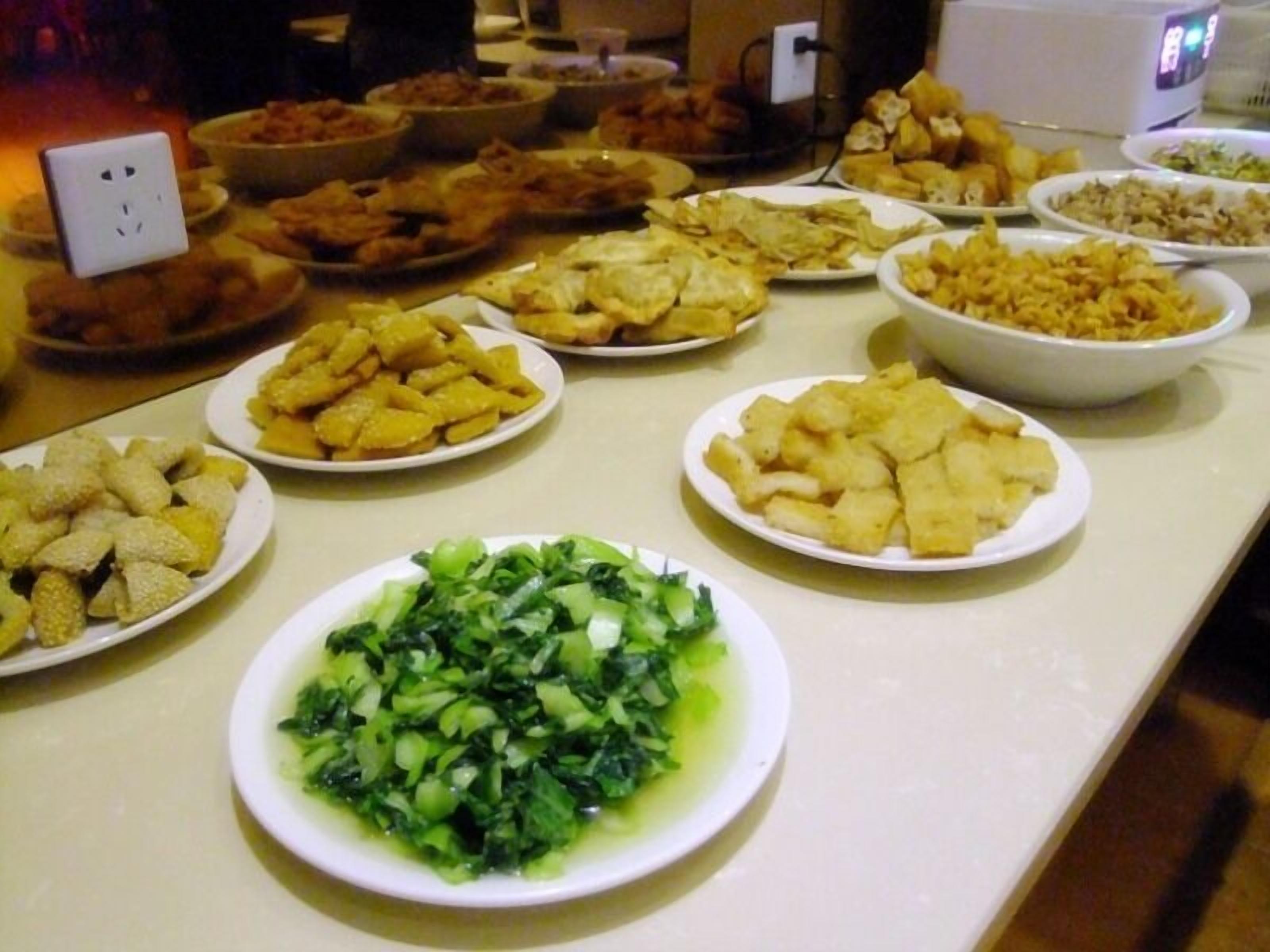 A buffet table with various dishes including fried items, salads, and a bowl of greens.