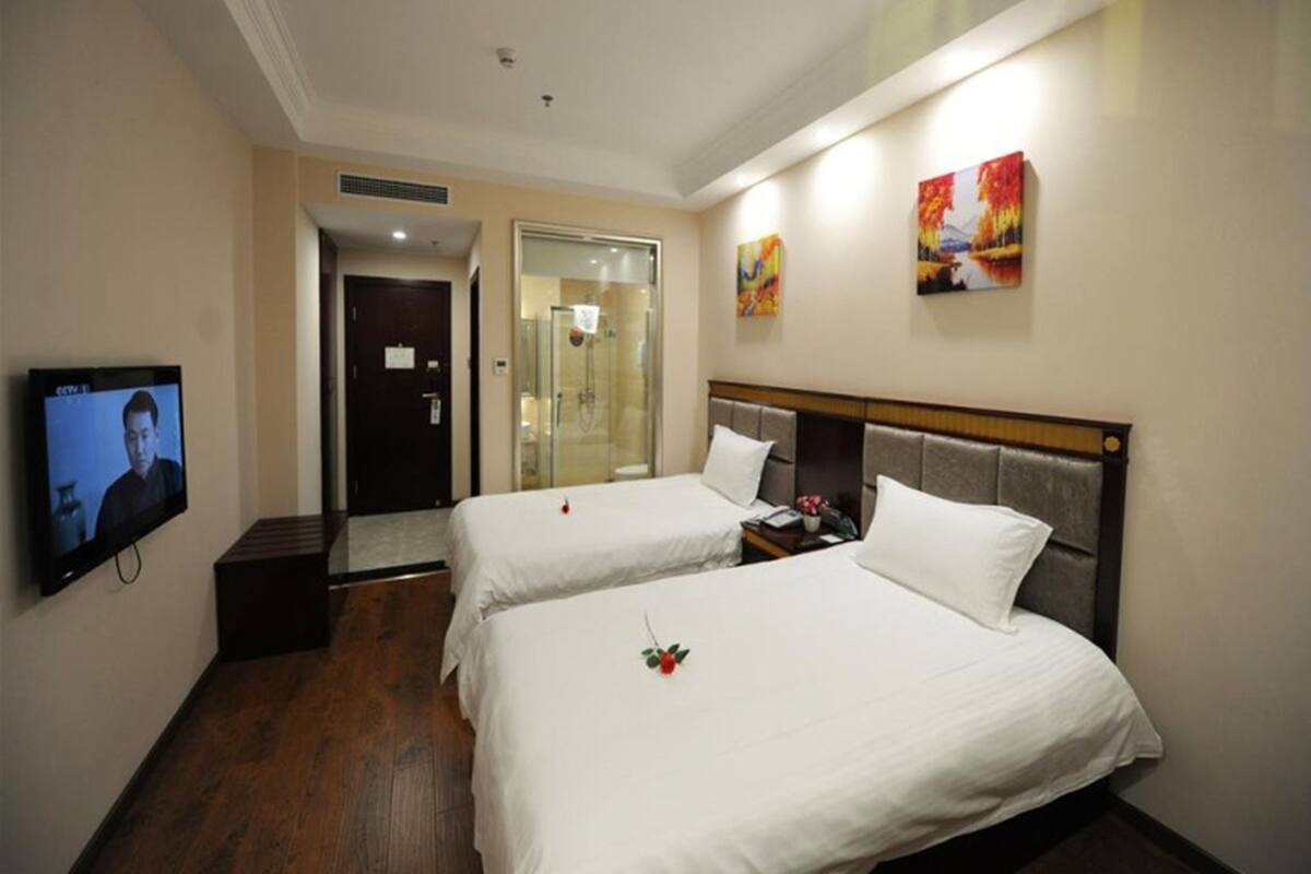 A hotel room with two beds, a TV, a shower, and artwork on the walls.