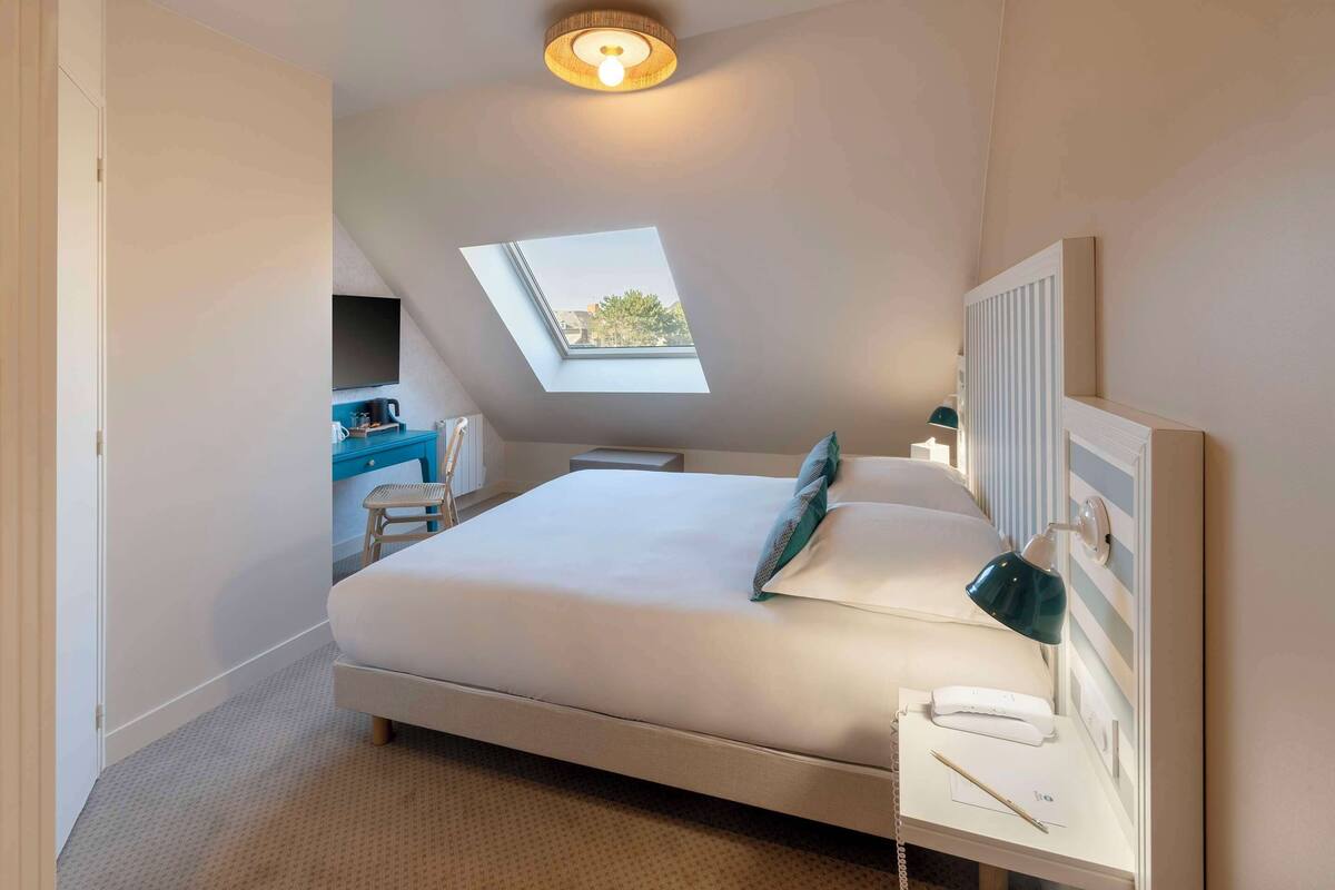 Een slaapkamer met dakraam, een bed, nachtkastje met lamp en klein bureau met stoel.