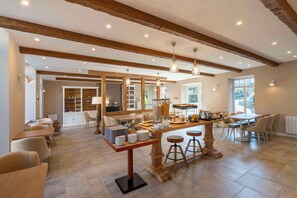 A spacious kitchen with wooden beams, a central island with stools, and a dining area with chairs.