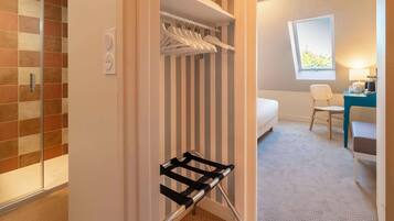 A hotel room with a walk-in closet, a bed, a desk with a chair, and a window.