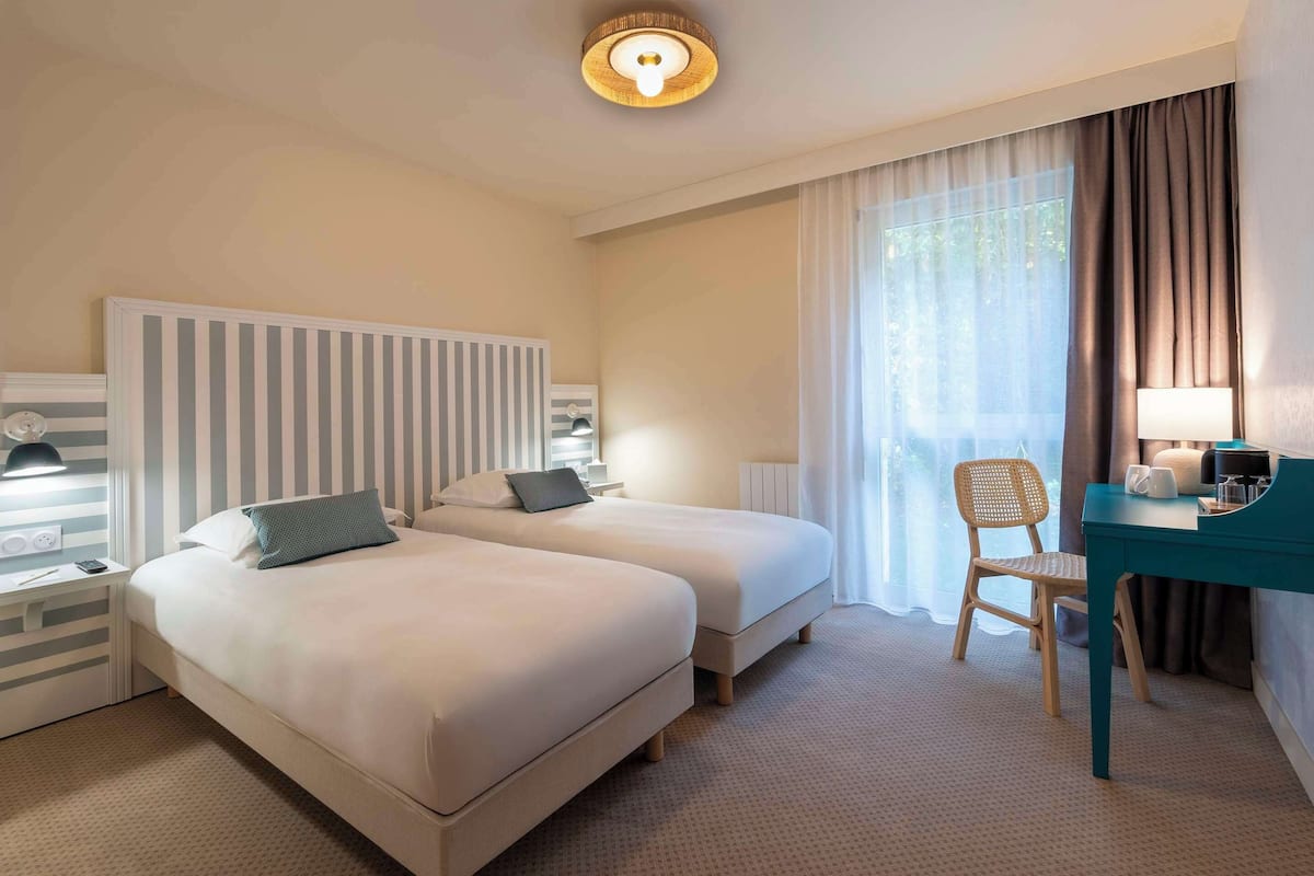 Een hotelkamer met twee bedden, een bureau, een stoel en een raam met gordijnen.