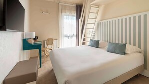Quarto de hotel com uma cama grande, uma escrivaninha com luminária, uma cadeira, televisão fixada na parede e uma janela com cortinas.