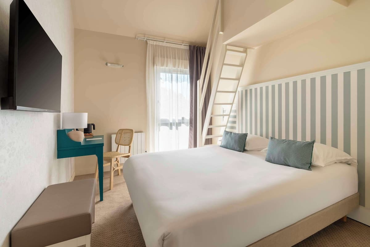Hotelkamer met een groot bed, bureau met lamp, stoel, televisie aan de muur en raam met gordijnen.