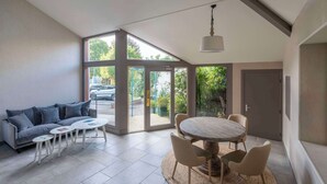 Uma sala de estar moderna com um sofá cinza, uma mesa de jantar redonda com cadeiras e uma grande janela com vista para o exterior.