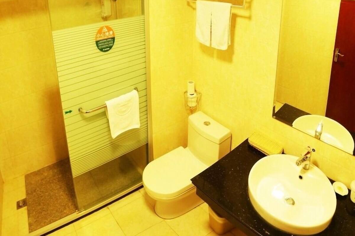 Une salle de bain équipée de toilettes, d’un lavabo et d’une douche. On y trouve un porte-serviettes avec des serviettes et un distributeur de savon.