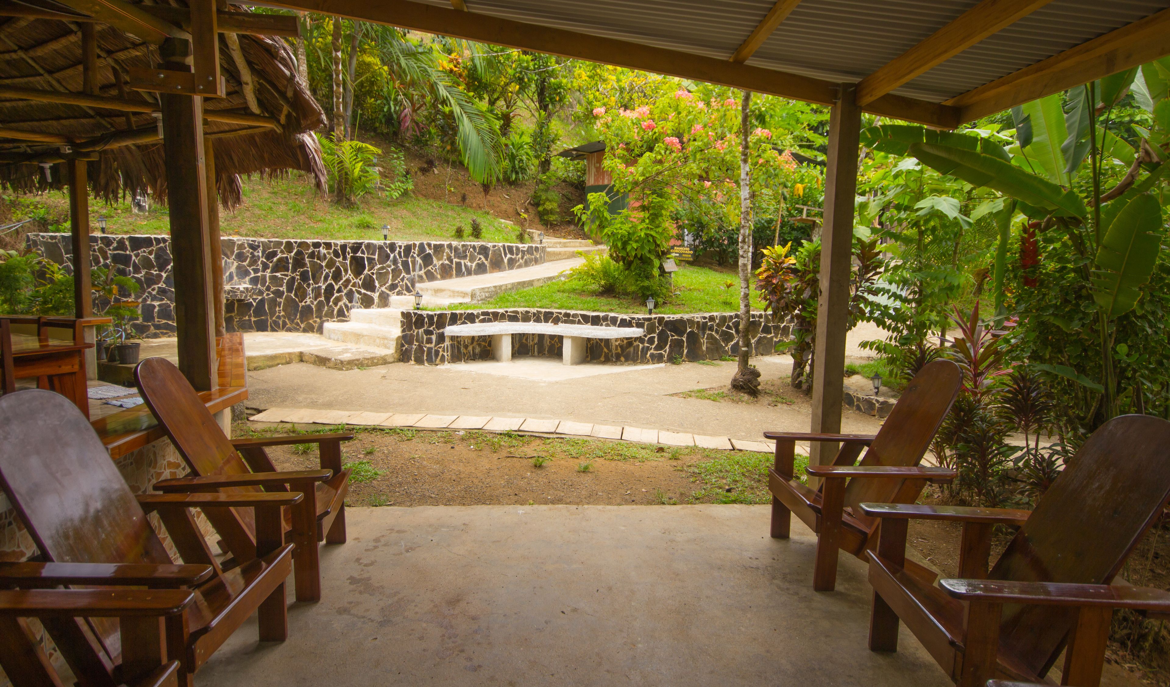 Un espacio de estar al aire libre cubierto, con paredes de piedra y un pequeño jardín.