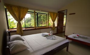 Ein Hotelzimmer mit einem großen Bett, zwei kleineren Betten, einer Holztür und einem Fenster mit Vorhängen.