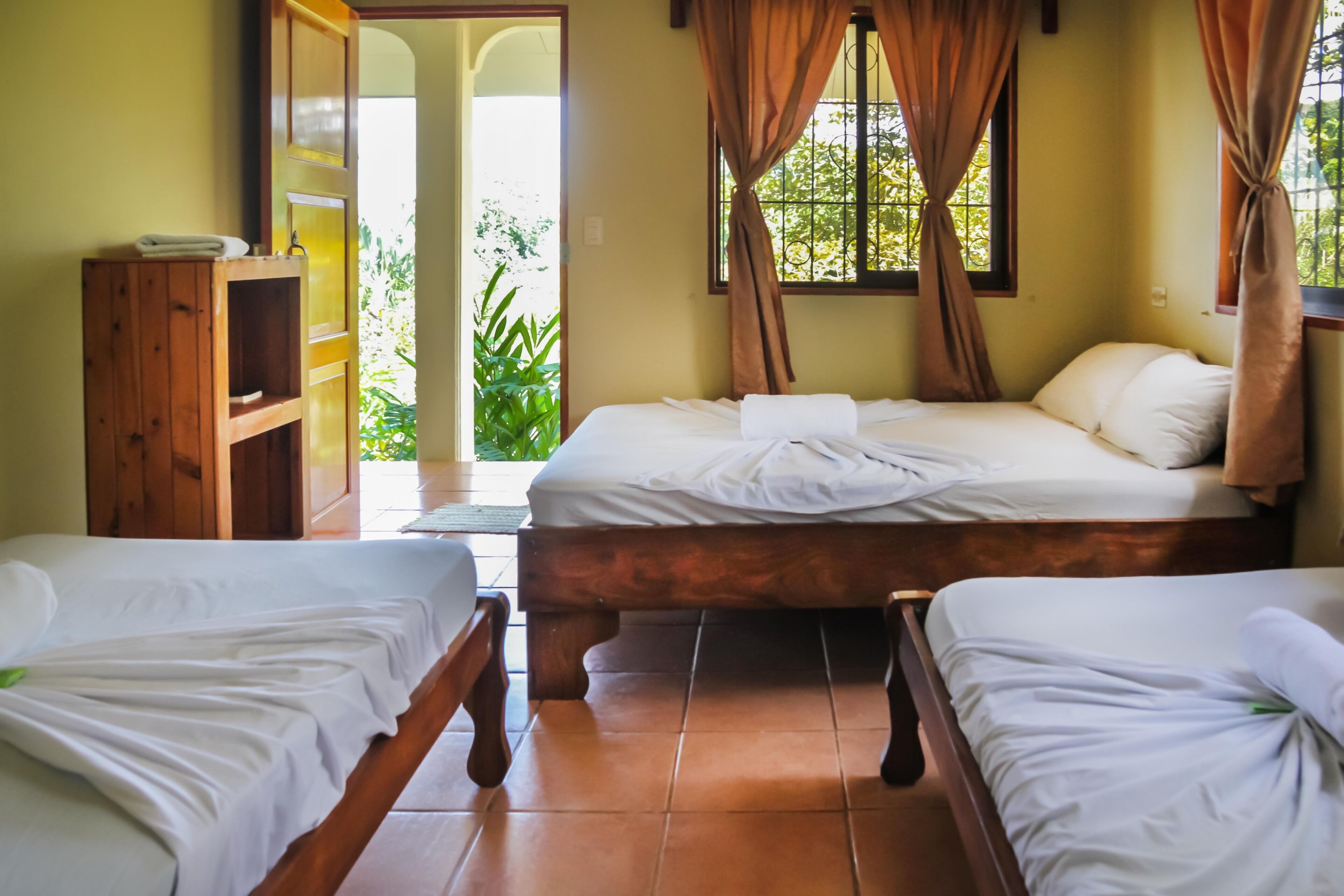 A room with two wooden beds, a wooden cabinet, and a view of greenery outside.