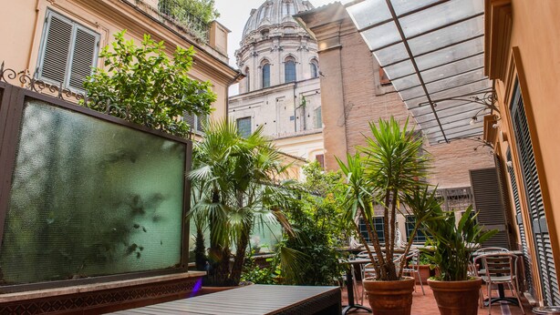 A courtyard with a glass enclosure, potted plants, and a view of a historic building with a dome. - Lh Royal Suites (Rome)