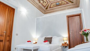 A hotel room with a large bed, a small table with a lamp, and a wooden door. - Lh Royal Suites (Rome)