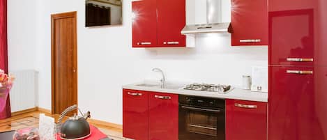 A modern kitchen with red cabinetry, a stainless steel range hood, a built-in oven, and a sink.