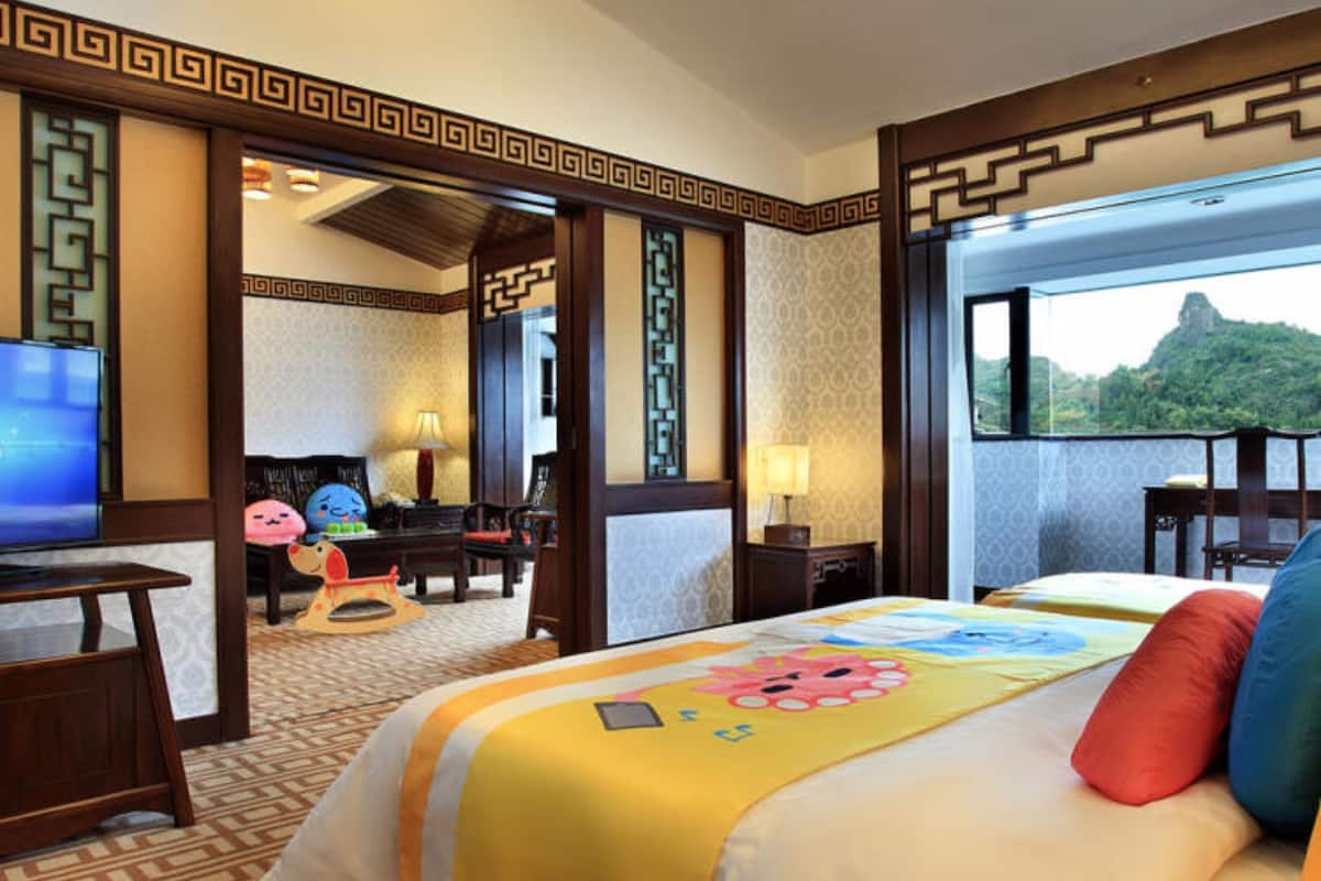 A hotel room with a large bed, a desk with a television, and a view of a mountain.